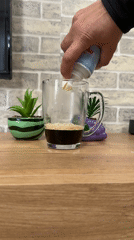 Person adds whipped cream to coffee mug on table