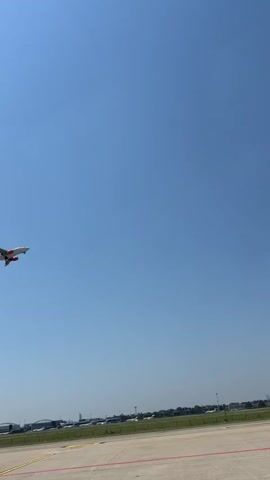 The video begins with a wide shot of a clear blue sky with a white airplane with orange accents taking off from an airport. The camera then zooms in on the tail of an orange and white airplane, showing the word "easy" on its side. Next, it shows a close-up of a person's feet walking down stairs, wearing a beige outfit and pink sneakers. Finally, it shows a close-up of another airplane's wing, also orange and white, with part of the word "easy" visible. The video appears to be filmed at an airport on a sunny day.