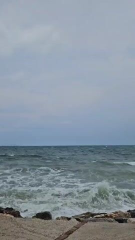 The video shows a choppy ocean with waves crashing against a rocky shore. The sky is overcast and gray, and the water is a deep blue-green. There are no people or animals visible in the video. The video is shot from a low angle, looking out at the ocean.