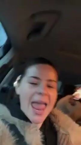 The video shows three women in a car, seemingly on a road trip, singing and dancing along to music. The camera begins by focusing on a woman in the back seat before panning to the driver, who is wearing glasses. The camera then returns to the back, where the woman is recording a video on her phone. All three women appear to be enjoying themselves.
