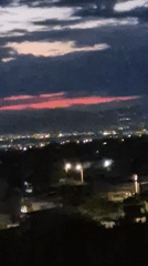 Nighttime cityscape recorded with pink-tinted clouds above scattered lights