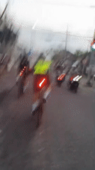 Cyclists roll through wet Mengwi streets on an overcast day