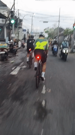 Cyclists roll through wet Mengwi streets on an overcast day