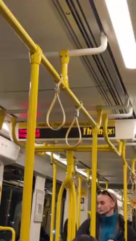 Here is a concise description of the video:

The video shows the inside of a tram with yellow poles and hanging straps. The next stop is displayed on a digital screen: "Clarendon St Junction". A woman with a blue jacket and a headband can be seen in the background. She glances around. It sounds like someone is talking, but the audio is unclear.