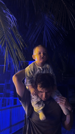 Father carries baby in dinosaur onesie on Đà Nẵng sidewalk