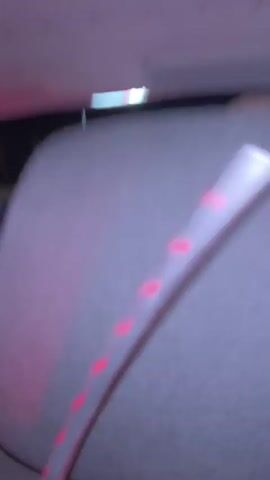 The video shows the interior of a car at night with colorful lights blinking. The driver is wearing a blue shirt and behind the passenger seat there is a LED strip of red lights. A person is seen holding a black object that appears to be a phone or tablet. The last shot shows two people laying down with the car lights changing colors. There is music playing.