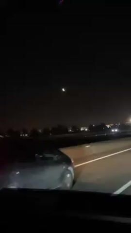 The video shows a car driving down a highway at night. The moon is visible in the sky, and there are other cars on the road. The view is from the inside of a car, and the dashboard is visible.