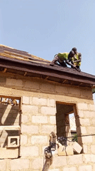 Workers install roofing shingles on cinder block building construction