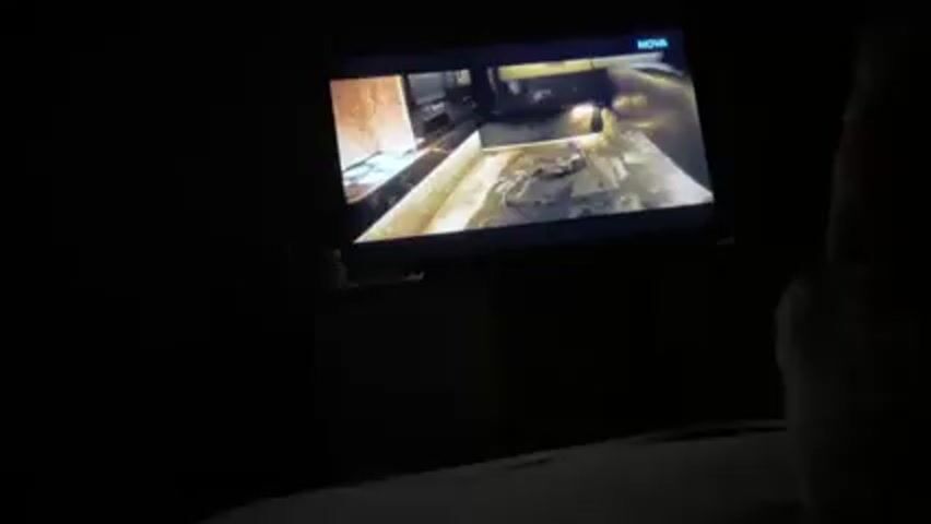 A television screen displays a close-up shot of a cluttered, stainless-steel surface, with what appears to be a remote control positioned in the foreground. The scene is darkly lit and the environment surrounding the television is also very dark. The television logo "NOVA" is visible in the upper right corner.