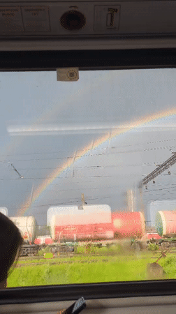 Rainbow over train yard, seen from a moving carriage window