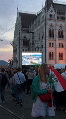 Evening crowd gathers at Hungarian Parliament with large screen display