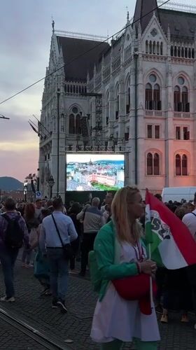 Evening crowd gathers at Hungarian Parliament with large screen display