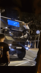 Evening street gathering involves military truck, palm tree rest