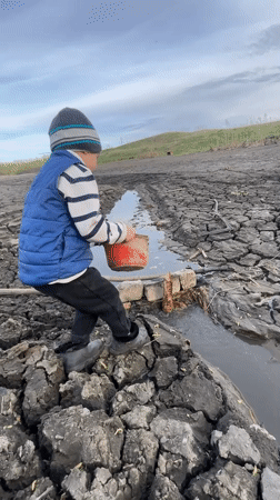 Boy places object in water channel amid cracked mudflats