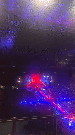Packed Milan arena concert, X-shaped stage, red and purple lights