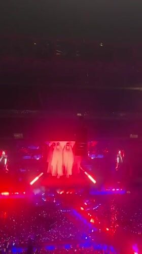 Packed Milan arena concert, X-shaped stage, red and purple lights