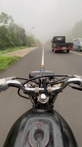 Motorcyclist navigates foggy road conditions in Karangmangu, Indonesia