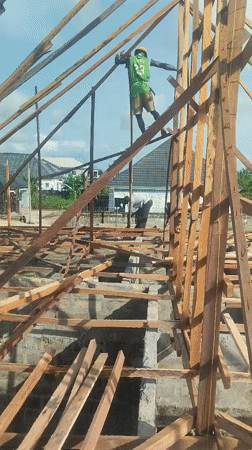 Construction workers frame building, one balancing on wooden beams