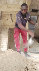 Construction worker shovels dirt in unfinished building, Nigeria