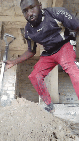 Construction worker shovels dirt in unfinished building, Nigeria