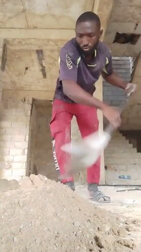 Construction worker shovels dirt in unfinished building, Nigeria