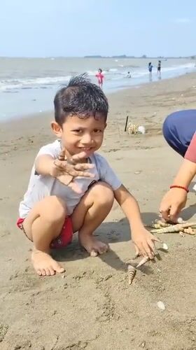 Kids play on a shell-scattered beach in Lhokseumawe
