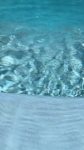 The video shows the surface of a swimming pool with light refracting through the water, creating patterns on the pool floor and walls. The water is clear and blue. The bottom of the pool appears to be made of white tiles or plaster. The lighting suggests it is daytime.