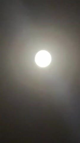 This video shows a progression of a bright, round light source against a dark background. Initially, the light appears to be a diffused glow with indistinct edges. As the video progresses, the light source becomes clearer and more defined, resolving into a circular object with visible texture and shading. The background gradually transitions from a lighter, smoky haze to a deep, uniform black, suggesting the transition from daytime or twilight to night, or perhaps from a lit interior to an exterior night sky. The object itself appears to be the moon, becoming increasingly detailed and illuminated as the video advances.