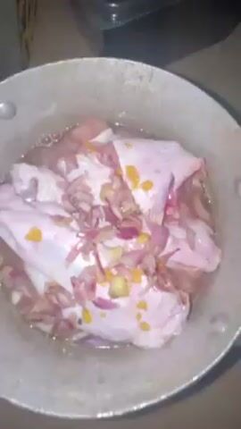 The video shows a saucepan sitting on what appears to be a stovetop. Inside the saucepan, there are several pieces of raw meat covered with chopped red onions and small pieces of what appear to be yellow peppers. There is also a clear liquid, possibly water, in the saucepan.