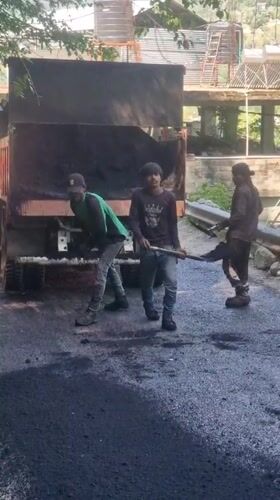 Road construction underway in Vashisht, India with workers spreading asphalt