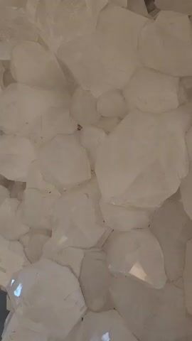 The video shows a close-up view of a cluster of white, opaque crystals. The crystals vary in size and shape, with many having sharp edges and flat surfaces. The overall texture appears rough and slightly uneven. There is light reflecting off some of the crystal surfaces. The camera is relatively still, maintaining a close focus on the crystal formation.
