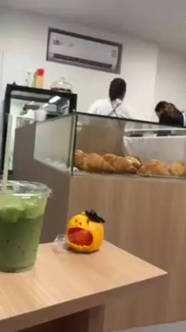 The video shows the interior of a cafe or bakery decorated for Halloween. 

Initially, the camera focuses on a display case filled with croissants.  A small, orange, stylized dog figure sits on a nearby table, next to a green drink. The camera then pans to the right, revealing two employees behind the counter.  One employee, with long brown hair, is bent over working, and a male employee in an apron stands to the side, adjusting his hair. 

The camera continues to pan further right, showing coffee cups stacked near a coffee machine.  Three jack-o'-lanterns of varying sizes are visible next to the machine. The final shot shows two fabric ghost figures, one wearing a witch's hat, positioned behind the jack-o'-lanterns, completing the Halloween scene. The cafe is well-lit with white walls, and Halloween decorations are hung on the walls.