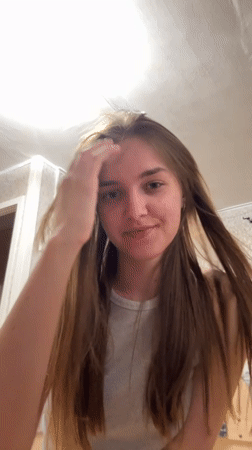 Woman adjusts hair, smiles indoors in Perm, Russia