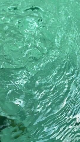 The video shows a close-up view of water, appearing turquoise. The water is slightly rippled, creating a textured surface. The light reflects on the water.