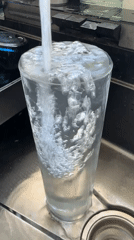 Person fills glasses with water in kitchen sink