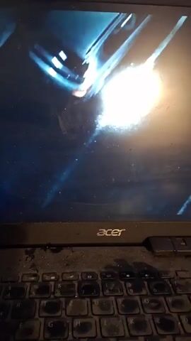 A laptop screen displays a blue, slightly grainy video. A bright white light is visible in the center and other similar lights move within the video. An Acer brand laptop is shown. The keyboard shows signs of wear.