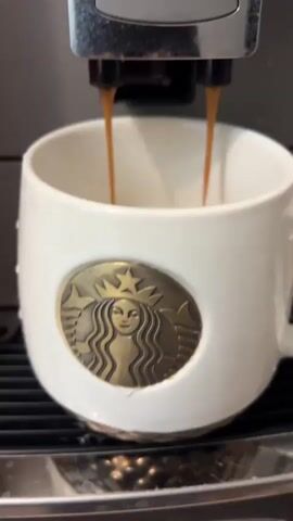 Here's a concise description of the video:

A Nivona espresso machine is dispensing espresso into a white Starbucks mug. Inside the mug are three white marshmallows. The hot espresso streams into the mug, partially covering the marshmallows.