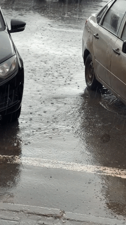 Rain soaks a street as cars navigate through puddles