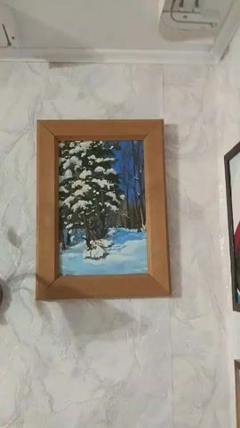 A painting of a snow-covered forest is hanging on a wall. The painting is framed in wood and depicts a large pine tree in the foreground, with smaller trees in the background. The ground is covered in snow, and the sky is blue. The painting appears to be old, as suggested by the date inscribed on it, which is difficult to read. The wall the painting is hanging on is covered in a patterned wallpaper.
