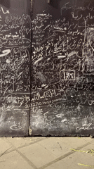 Dense chalk graffiti in Arabic and Hebrew script covers a Tehran wall.