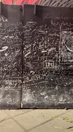 Dense chalk graffiti in Arabic and Hebrew script covers a Tehran wall.