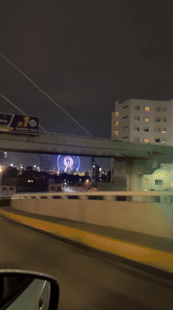 Illuminated Ferris wheel spotted under highway overpass in Puebla