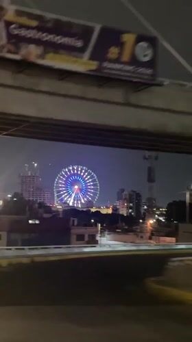 Illuminated Ferris wheel spotted under highway overpass in Puebla