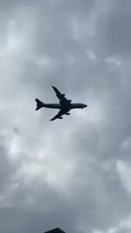 The video shows a large airplane silhouetted against a cloudy sky. The plane is in flight, appearing to be descending. A streetlight is visible in the foreground of the video, appearing at the lower-right of the frame.