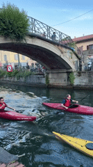 Kayakers paddle through Milan canal under bridge