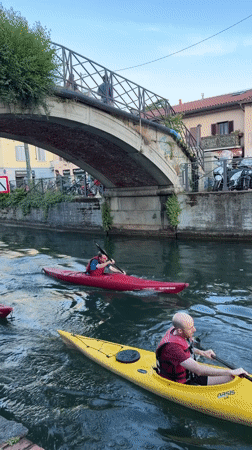 Kayakers paddle through Milan canal under bridge