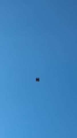 The video shows a black drone flying in a clear, bright blue sky. The drone is positioned in the center of the frame. The drone moves higher and lower during the video.