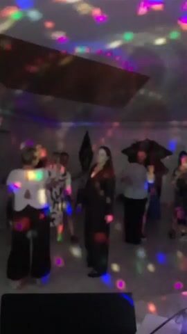 A group of people are dancing in a dimly lit room. Colorful lights are projected onto the ceiling and walls, creating a disco-like atmosphere. Some people are dancing individually, while others are dancing in pairs. The people appear to be enjoying themselves.