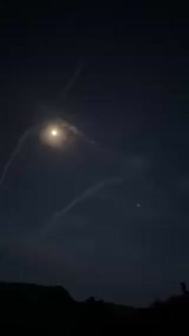 The video shows a night sky with a bright moon and contrails from aircraft. The trails appear as white lines against the dark blue sky. There are also some trees or a hill silhouetted at the bottom of the frame.