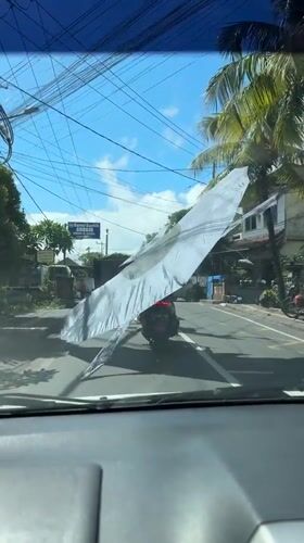 Motorcyclist carries oversized banner on Denpasar street